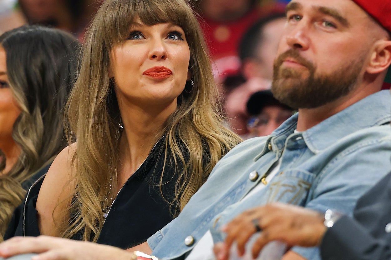People seated at a sports event. Woman with bangs in elegant attire, man beside her in casual outfit with cap. Others next to them also watching