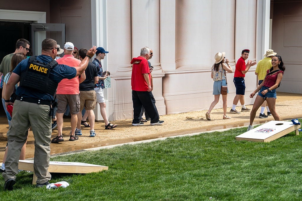 People playing cornhole outdoors astatine an event, with a constabulary serviceman interacting and different attendees watching oregon walking by