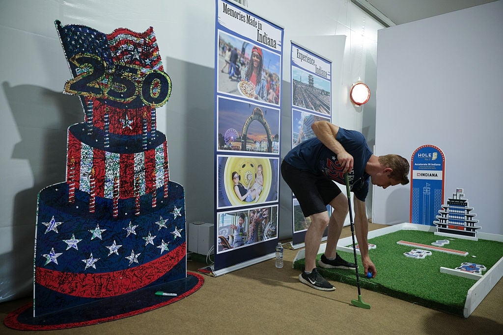 Person playing mini-golf indoors beside a ample 250-themed decoration and informational posters