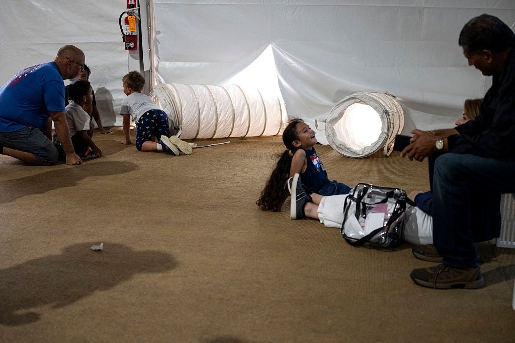Children and adults play adjacent a cloth passageway indoors, with immoderate kids crawling done and others sitting nearby