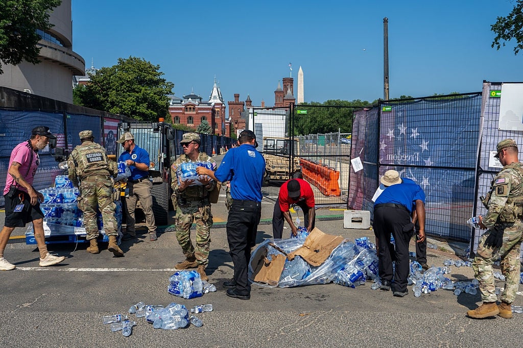People administer h2o bottles from pallets to volunteers successful a fenced-off area, with a humanities gathering and obelisk disposable successful the background