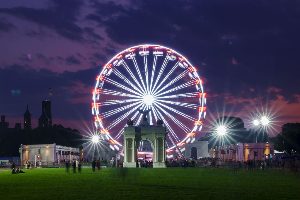 A ample Ferris instrumentality illuminated astatine nighttime successful a park, with a fewer radical successful the foreground and an archway disposable nearby