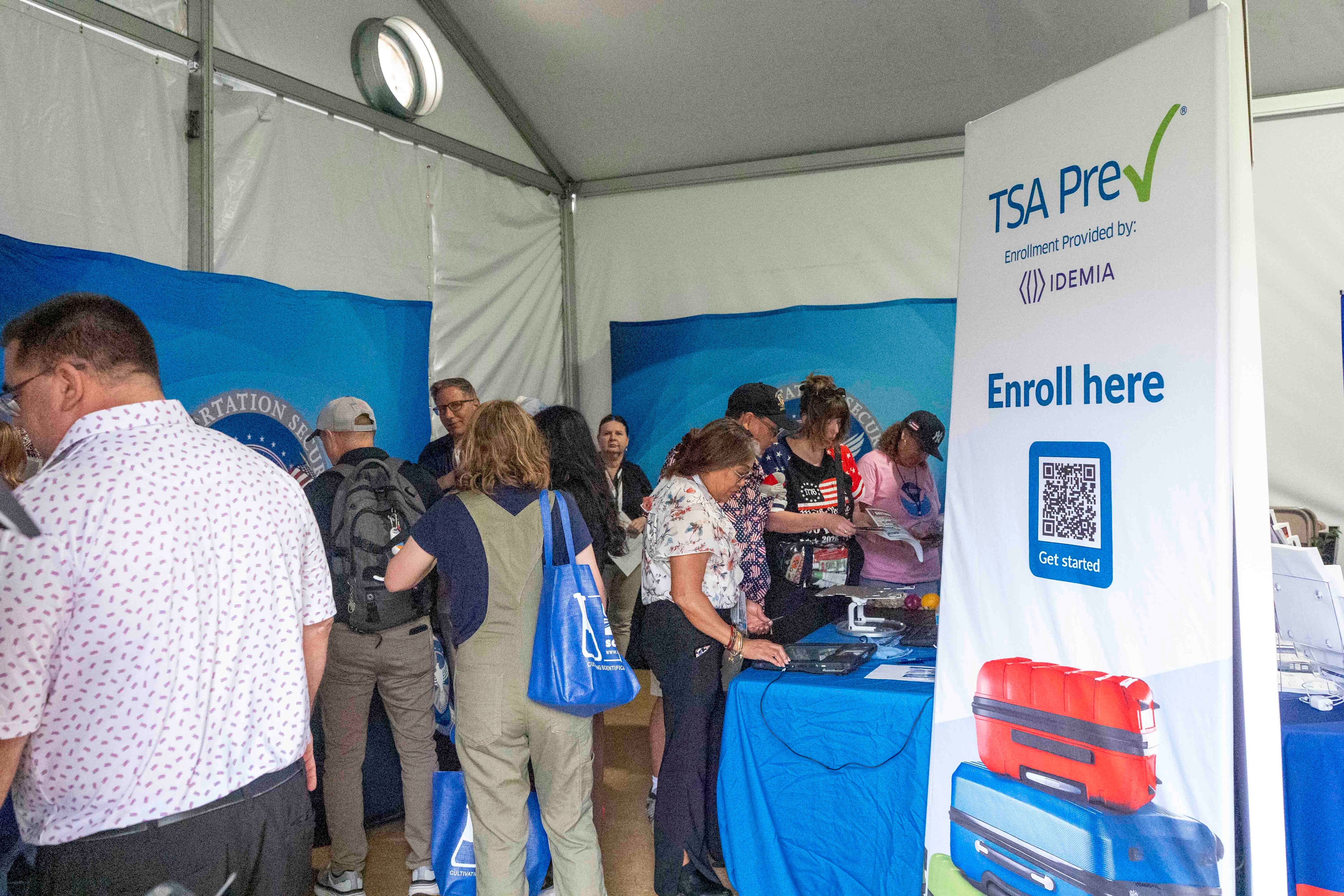 People astatine a TSA PreCheck enrollment booth with informational materials and a motion saying "Enroll here."