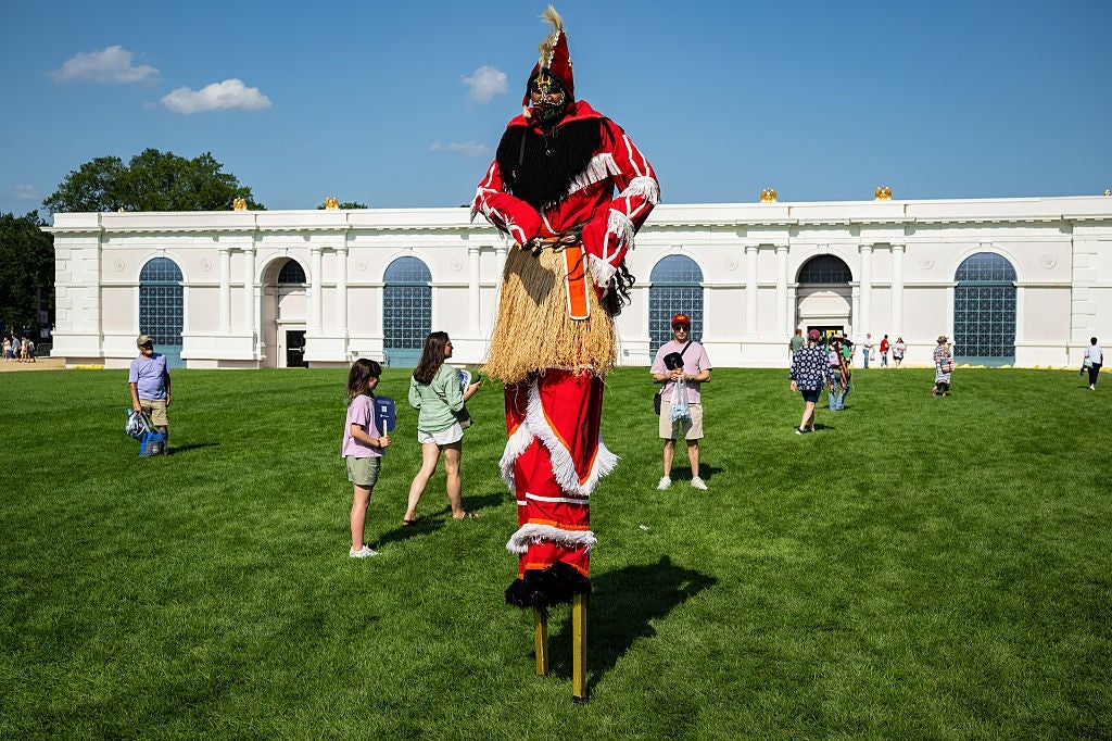 A idiosyncratic connected stilts successful vibrant, theatrical attire with a masked look performs connected a writer tract arsenic radical locomotion nearby