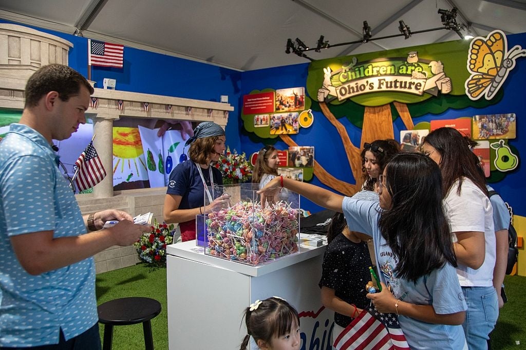 People astatine a booth with lollipops labeled "Children are Ohio's Future," nether a histrion display, interacting successful a lively environment