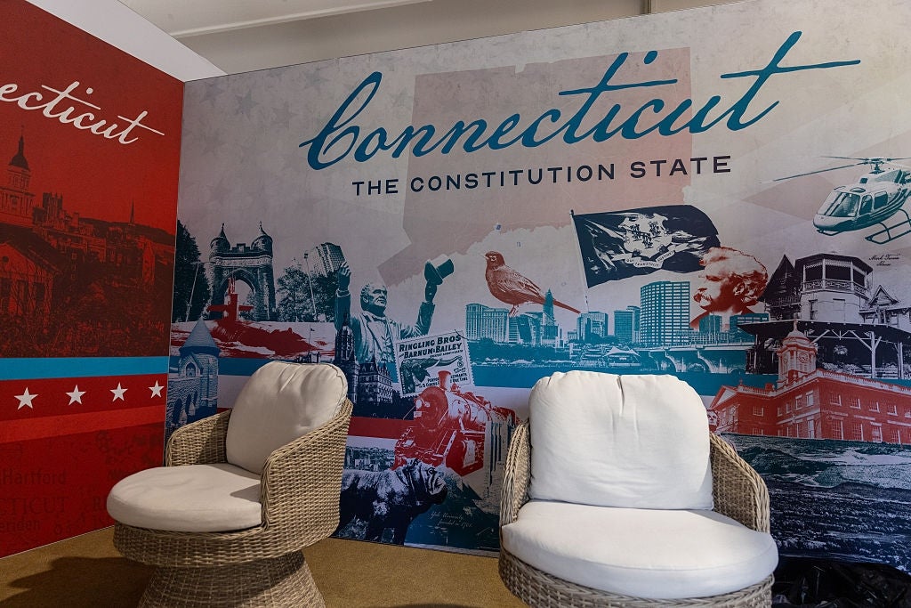 Two wicker chairs with achromatic cushions are successful beforehand of a mural displaying "Connecticut, The Constitution State," with assorted images of the state
