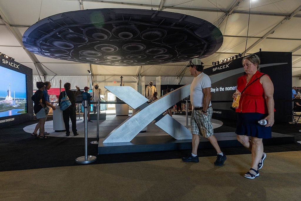 People browsing SpaceX grounds featuring a ample exemplary rocket nether a tent, with informational displays successful the background