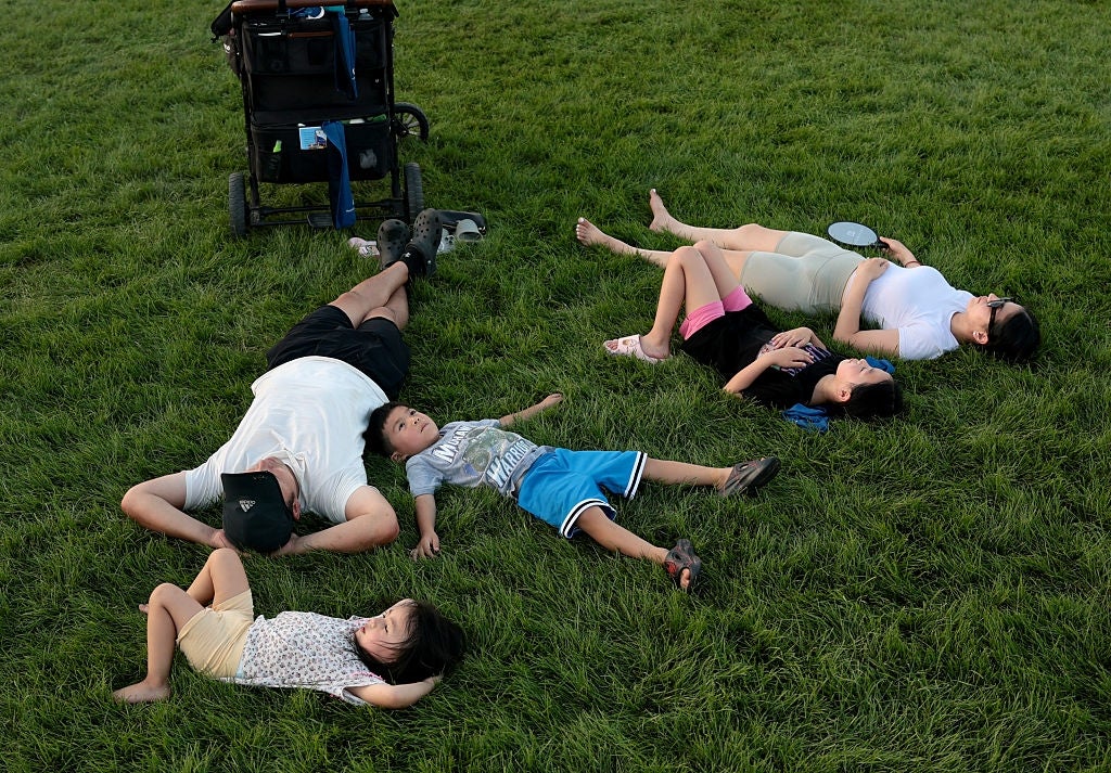 A household of 5 relaxes connected a grassy tract adjacent a stroller, lying connected their backs with arms and legs outstretched