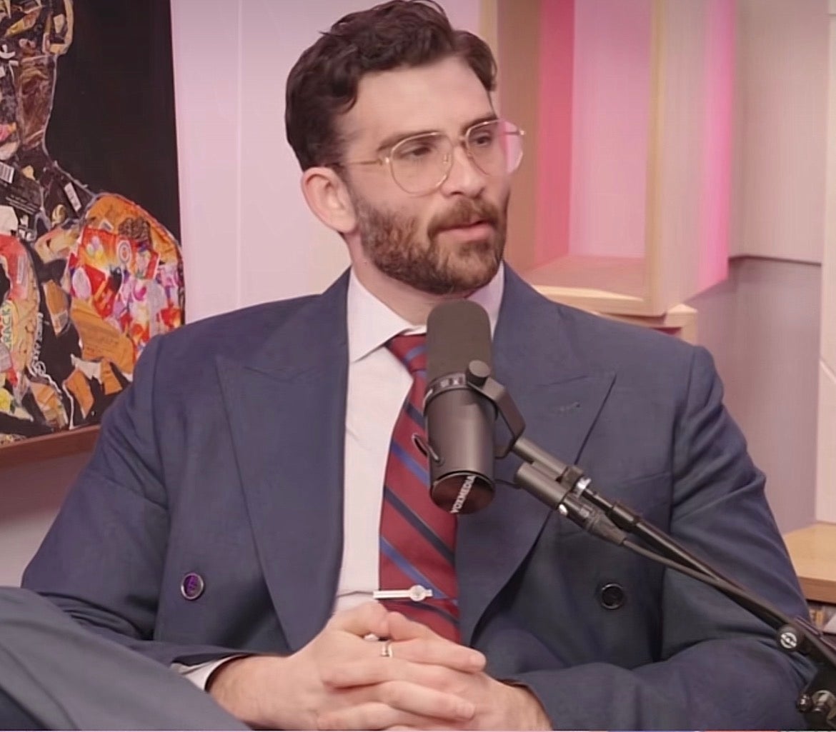 Person successful a suit with glasses speaking into a microphone during a podcast oregon interview. Abstract creation is disposable successful the background