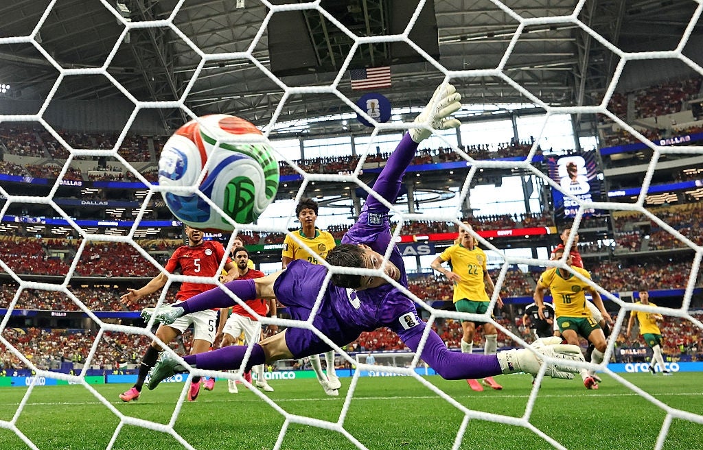 Fotballspiller i lilla uniform dykker for å redde når ballen treffer nettet under en fullsatt kamp på et stadion