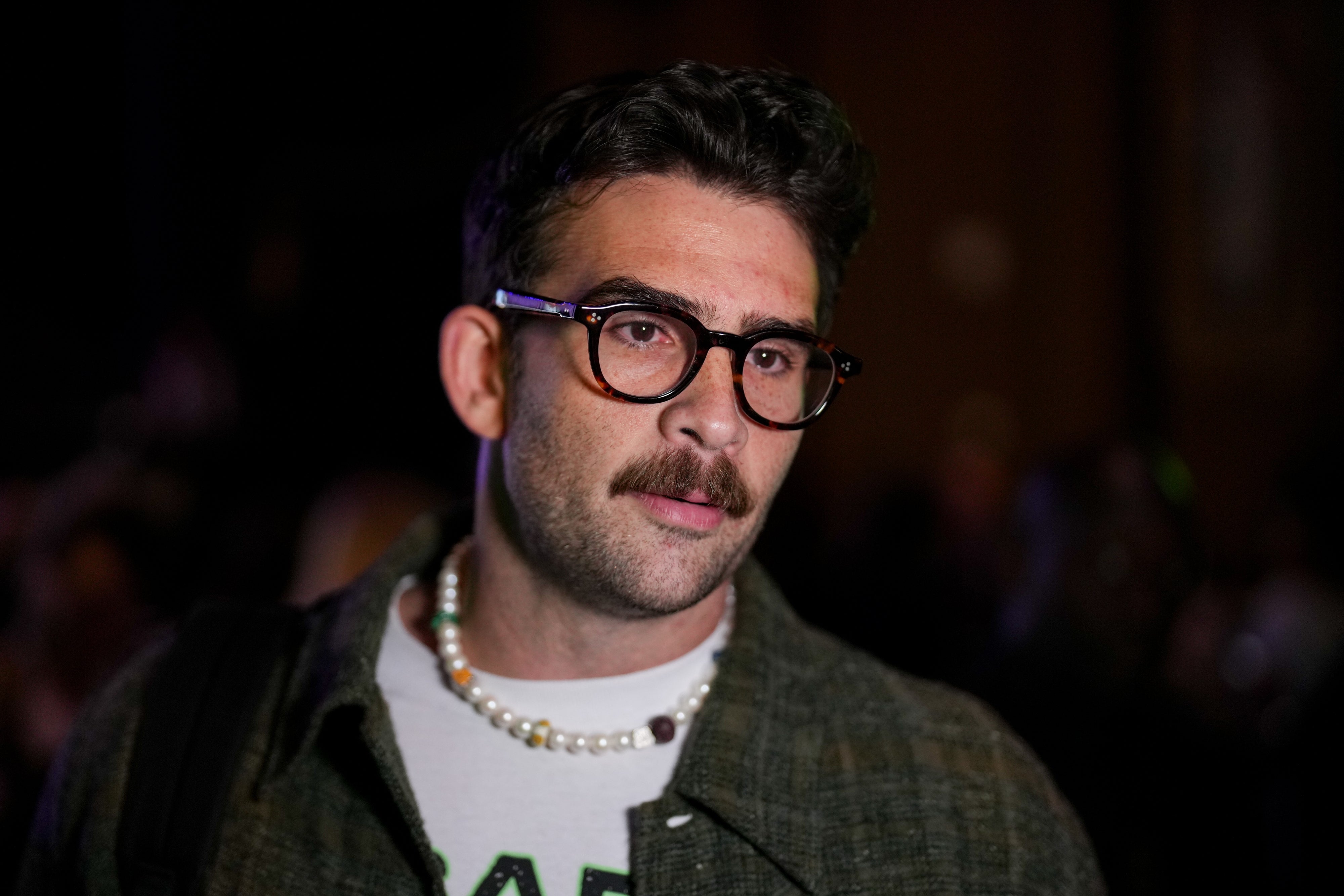 A idiosyncratic wearing glasses, a pearl necklace, and a patterned overgarment implicit a T-shirt astatine an event
