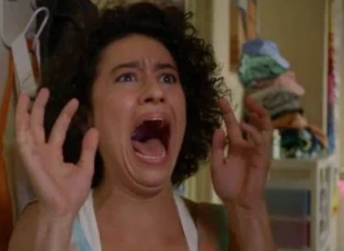 Person with curly hairsbreadth  expressing daze  oregon  excitement with wide   unfastened  rima  and raised hands. Background shows indoor mounting  with clothes