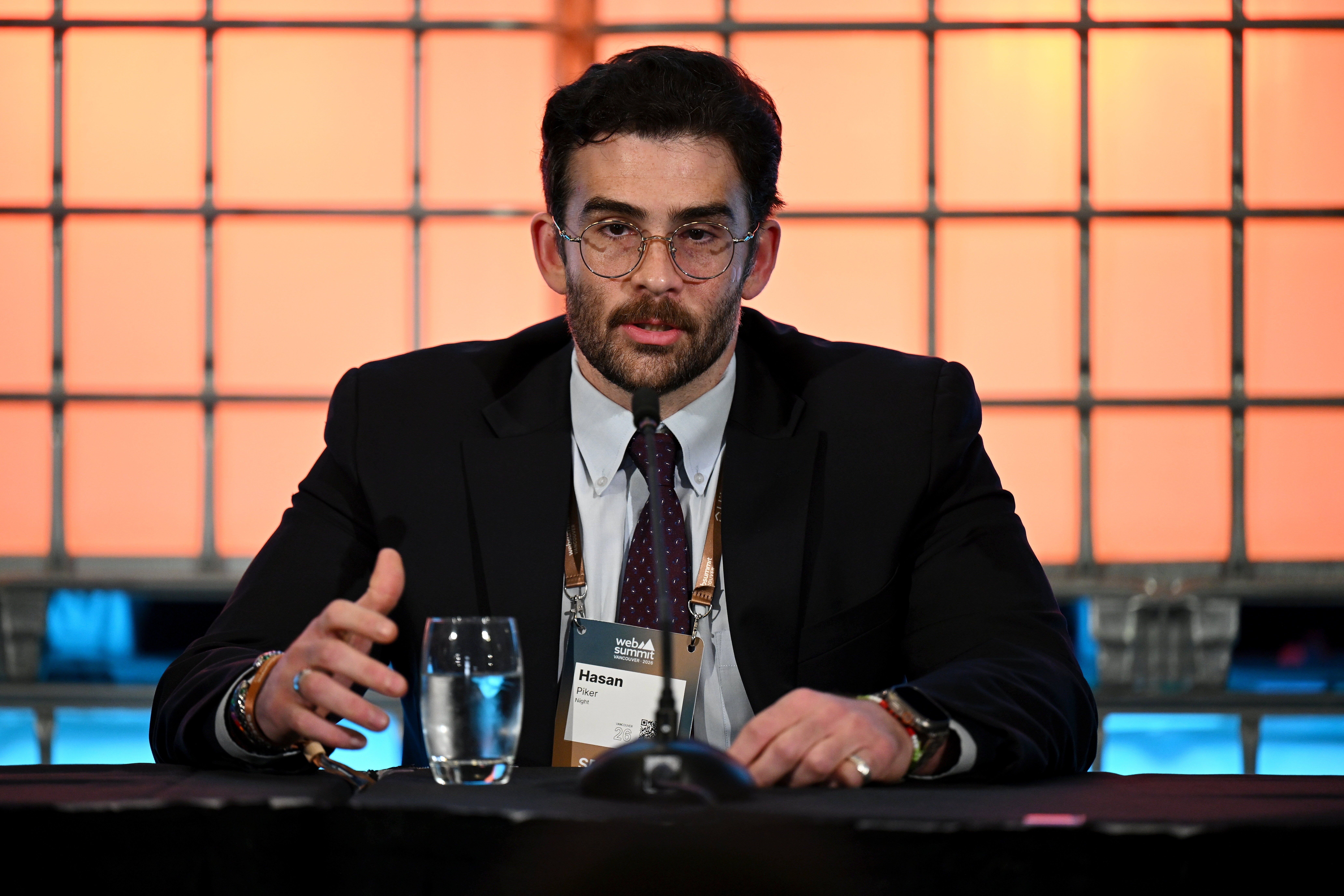 A idiosyncratic successful a suit and necktie speaks astatine a sheet discussion, seated down a microphone with a solid of h2o connected the table