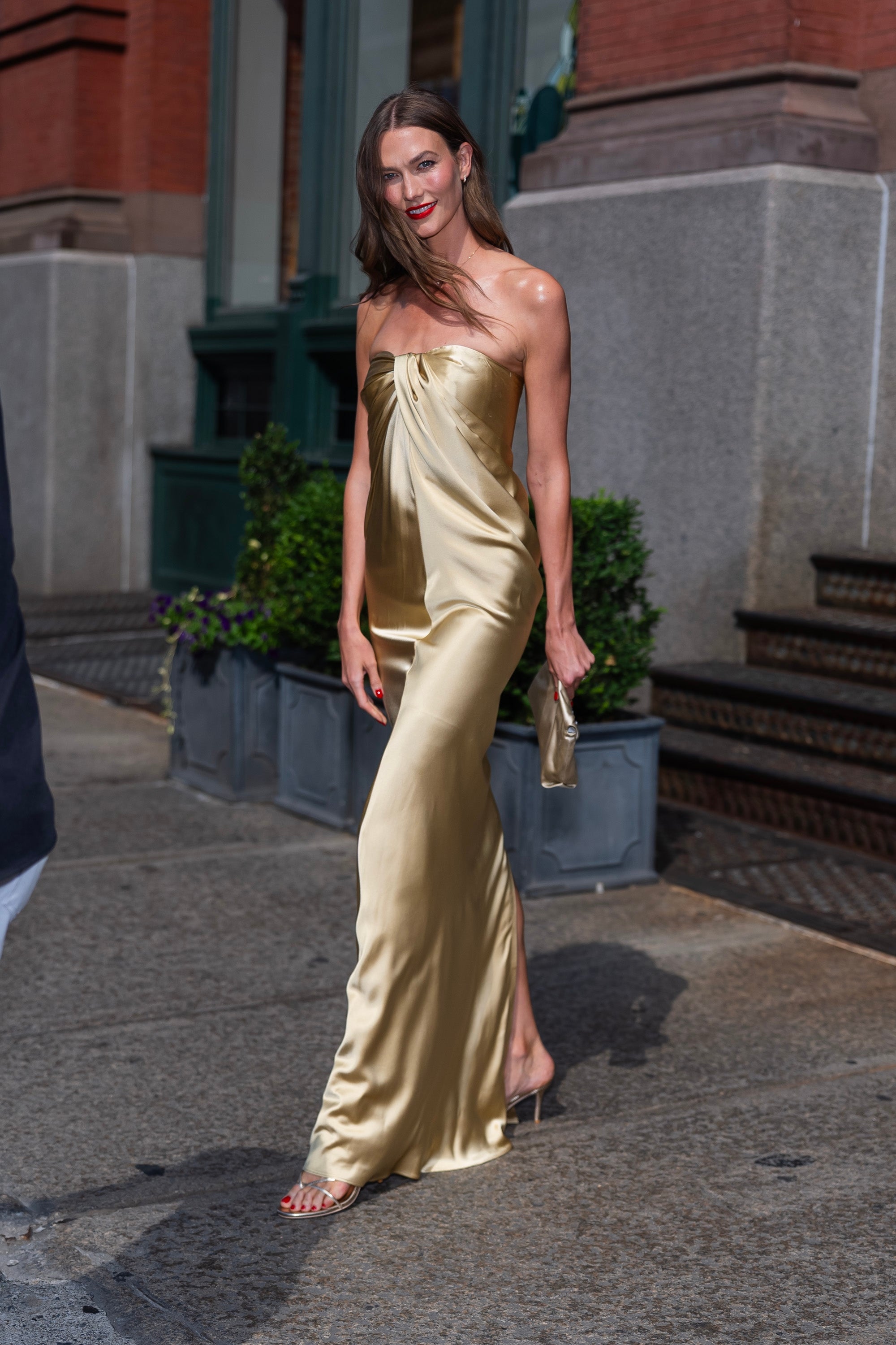 Person successful  a strapless, floor-length satin gown holding a clutch, walking outdoors