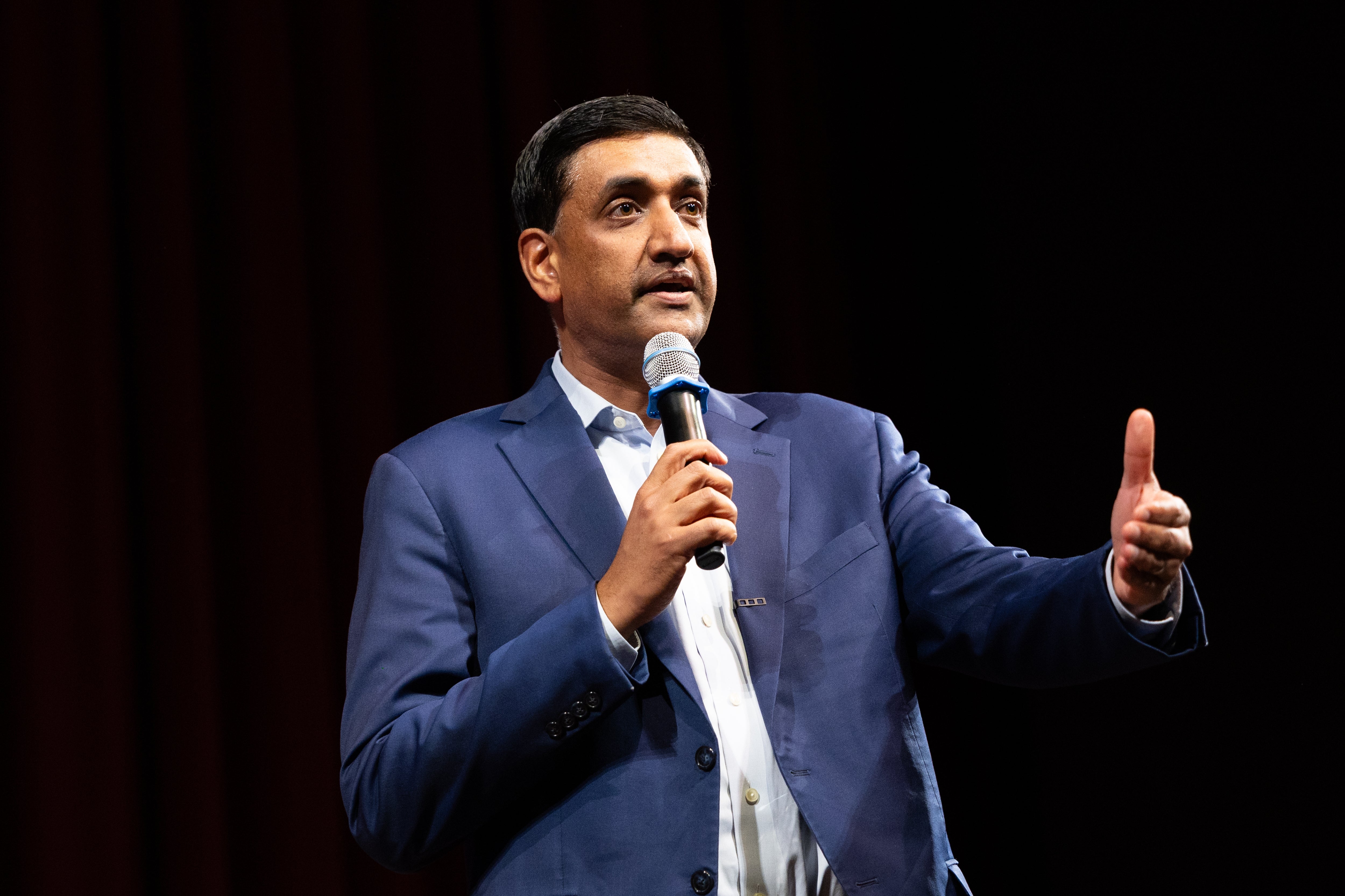 Person successful a suit speaking into a microphone connected stage, gesturing with 1 hand