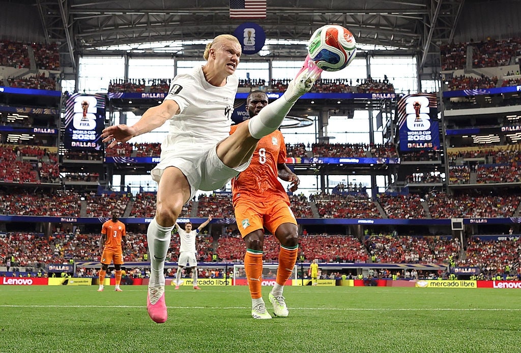 Fotballspiller utfører et høyt spark nær målet under en kamp, ​​med en motstander i nærheten og et stadionpublikum i bakgrunnen