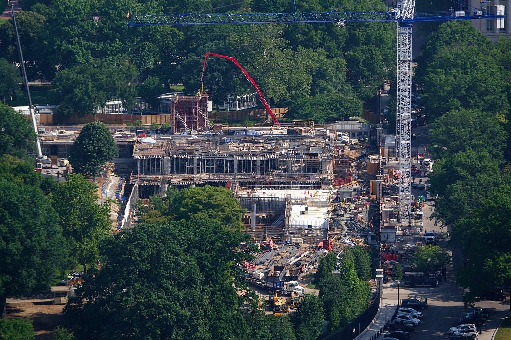 Luftfoto av en aktiv byggeplass omgitt av trær, med kraner og maskiner synlig, som indikerer byutvikling