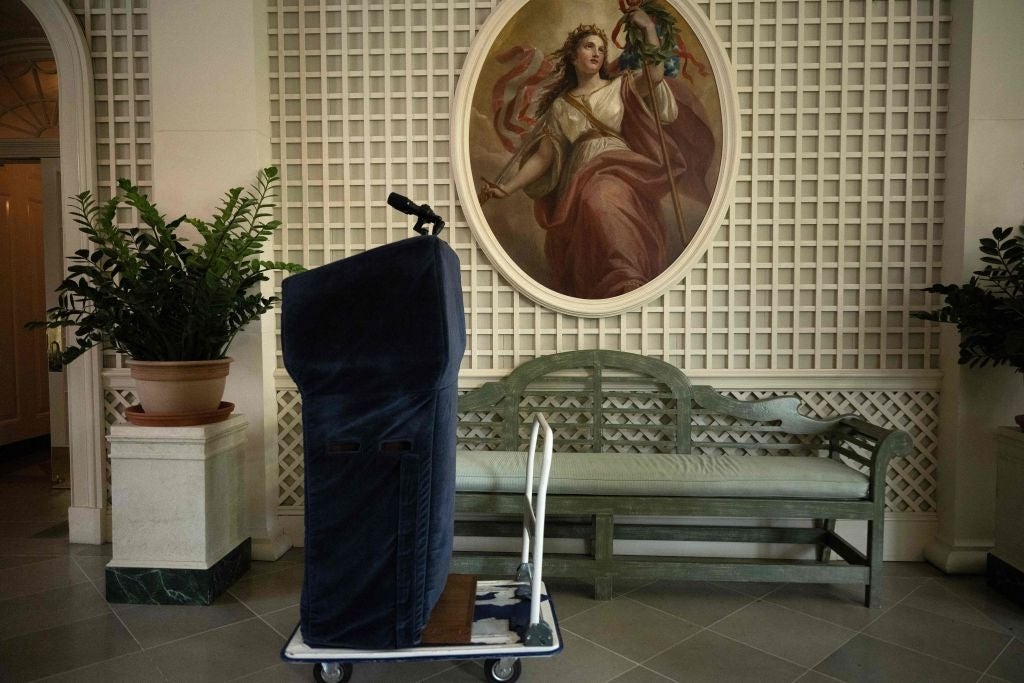 Dekket podium på en tralle i en lobby med et klassisk maleri av en kvinne som holder et septer i bakgrunnen; planter og sitteplasser i nærheten