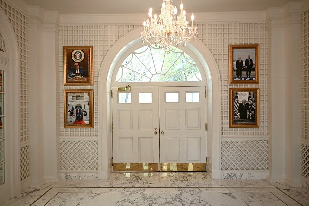 Elegant lobby med lysekrone, marmorgulv og innrammede bilder på vegger som flankerer en stor buet døråpning