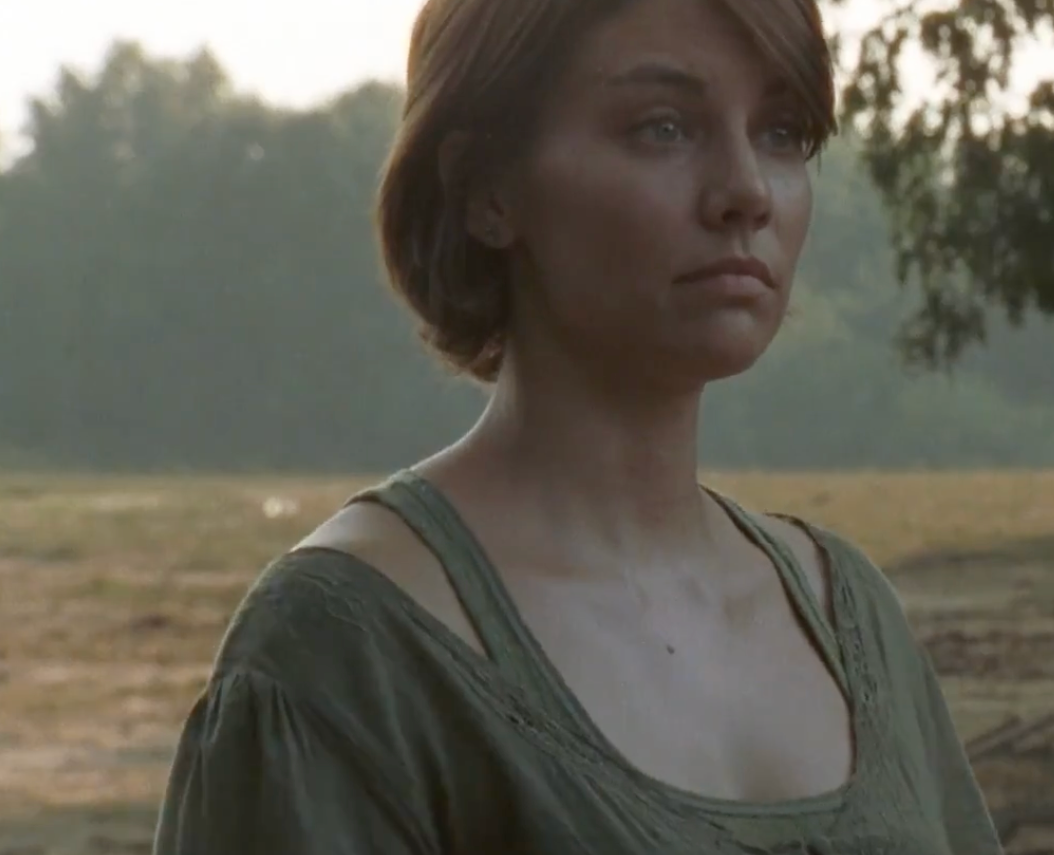 A person outdoors wearing a simple, casual top, looking thoughtful in a rural setting
