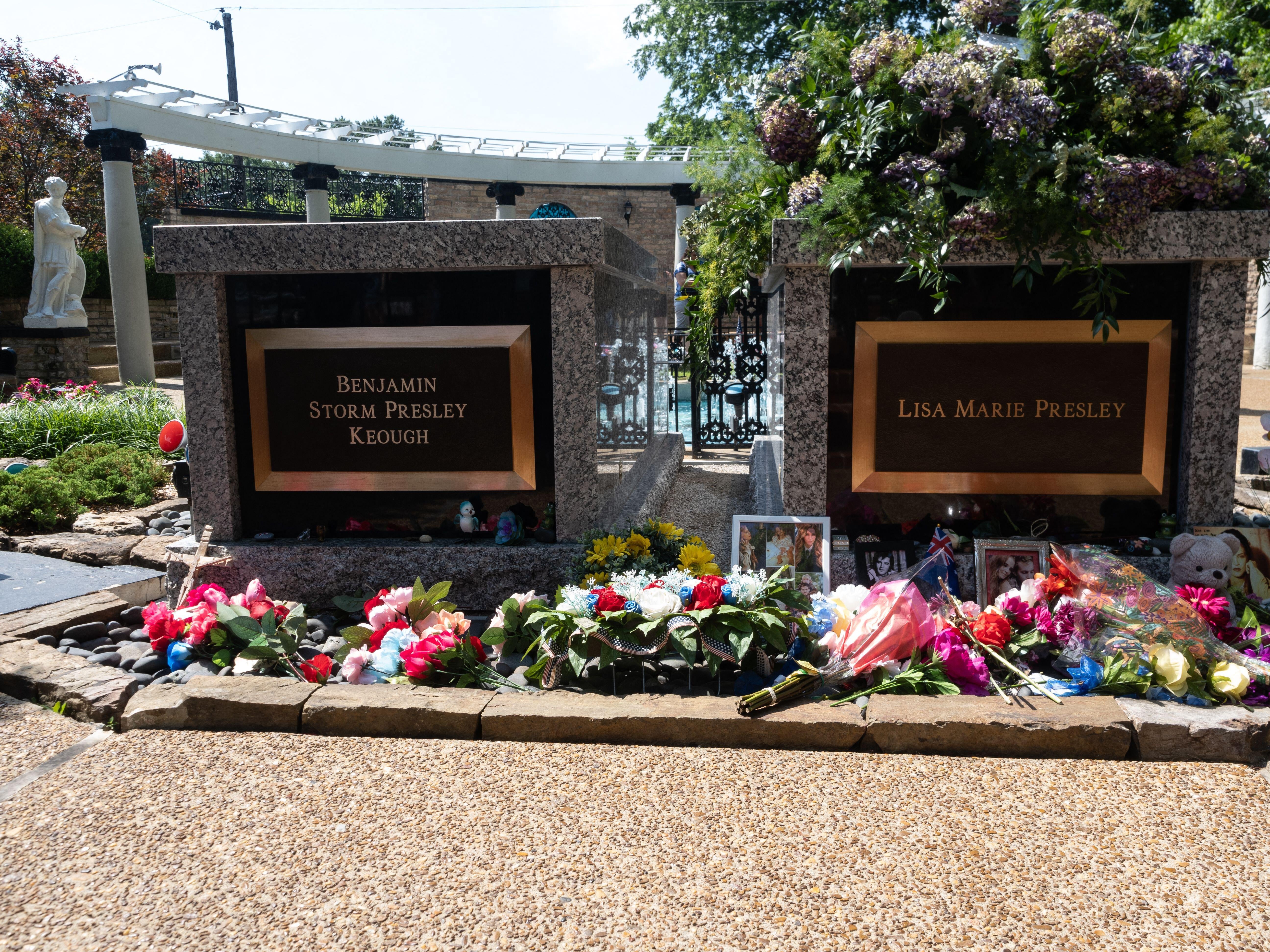 Two memorial plaques for Benjamin Storm Presley Keough and Lisa Marie Presley, surrounded by assorted flowers and tribute items