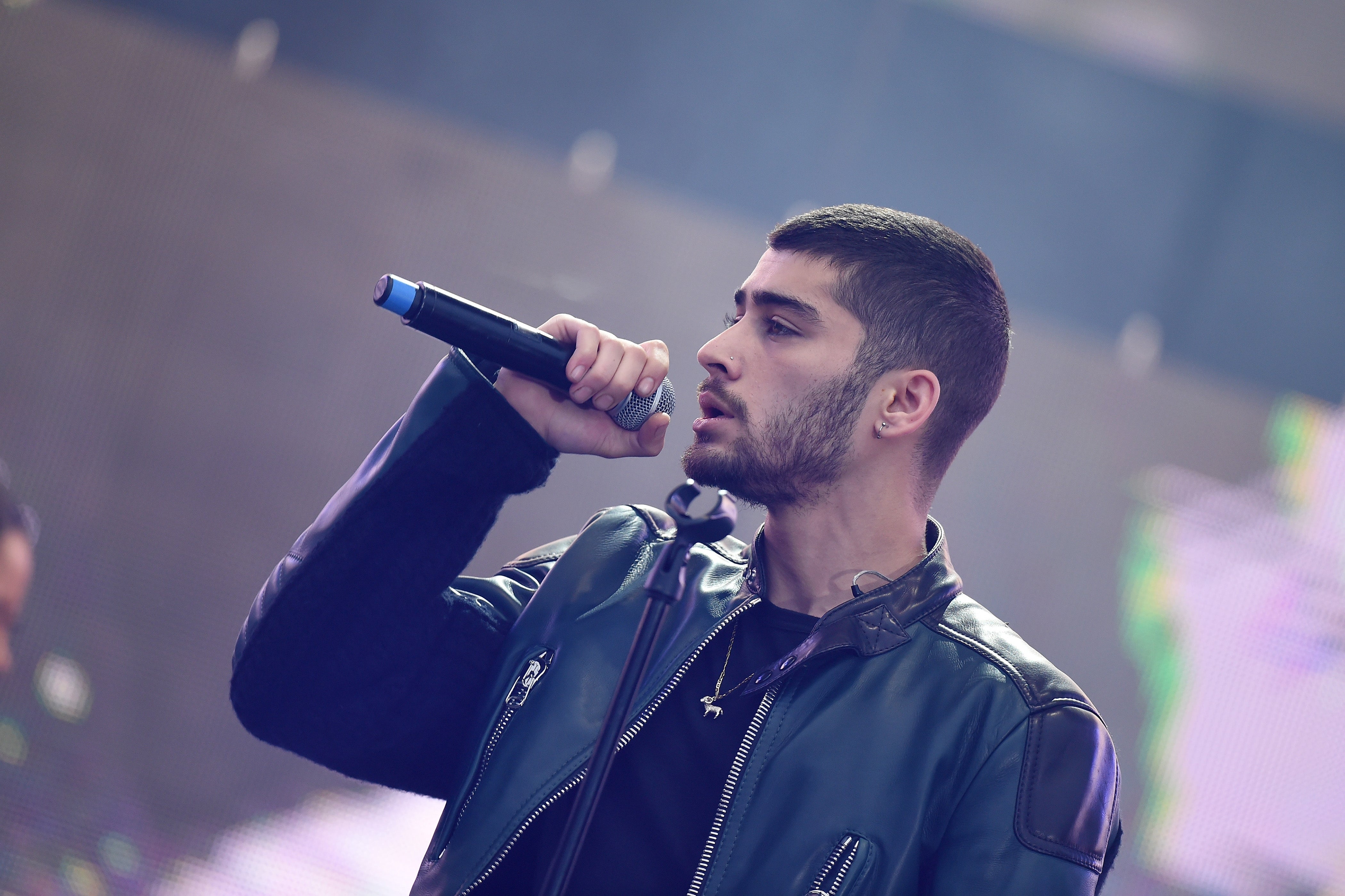 A singer on stage holding a microphone, wearing a leather jacket, performing energetically