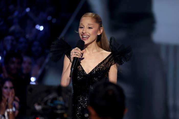 Person on stage in an elegant black dress holding a microphone and speaking to an audience
