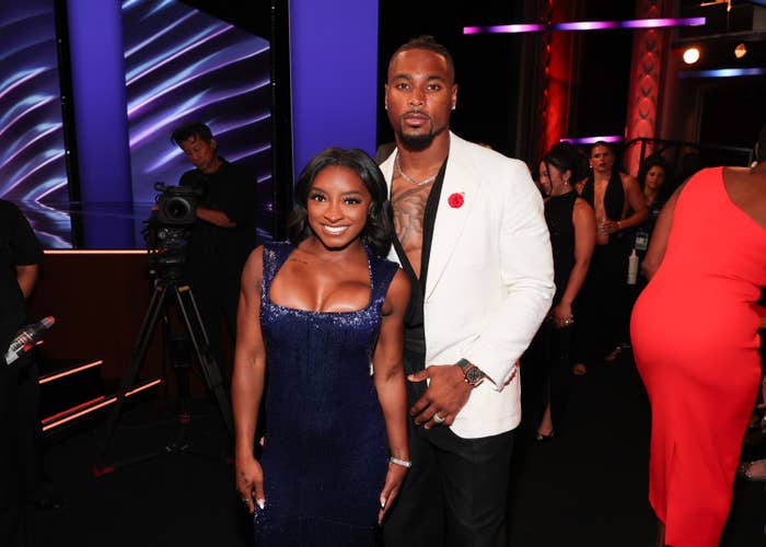 A personage  mates  poses connected  a reddish  carpet. The pistillate   wears a sleeveless, fitted gown, and the antheral   wears a achromatic  blazer implicit    a bare thorax  with tattoos