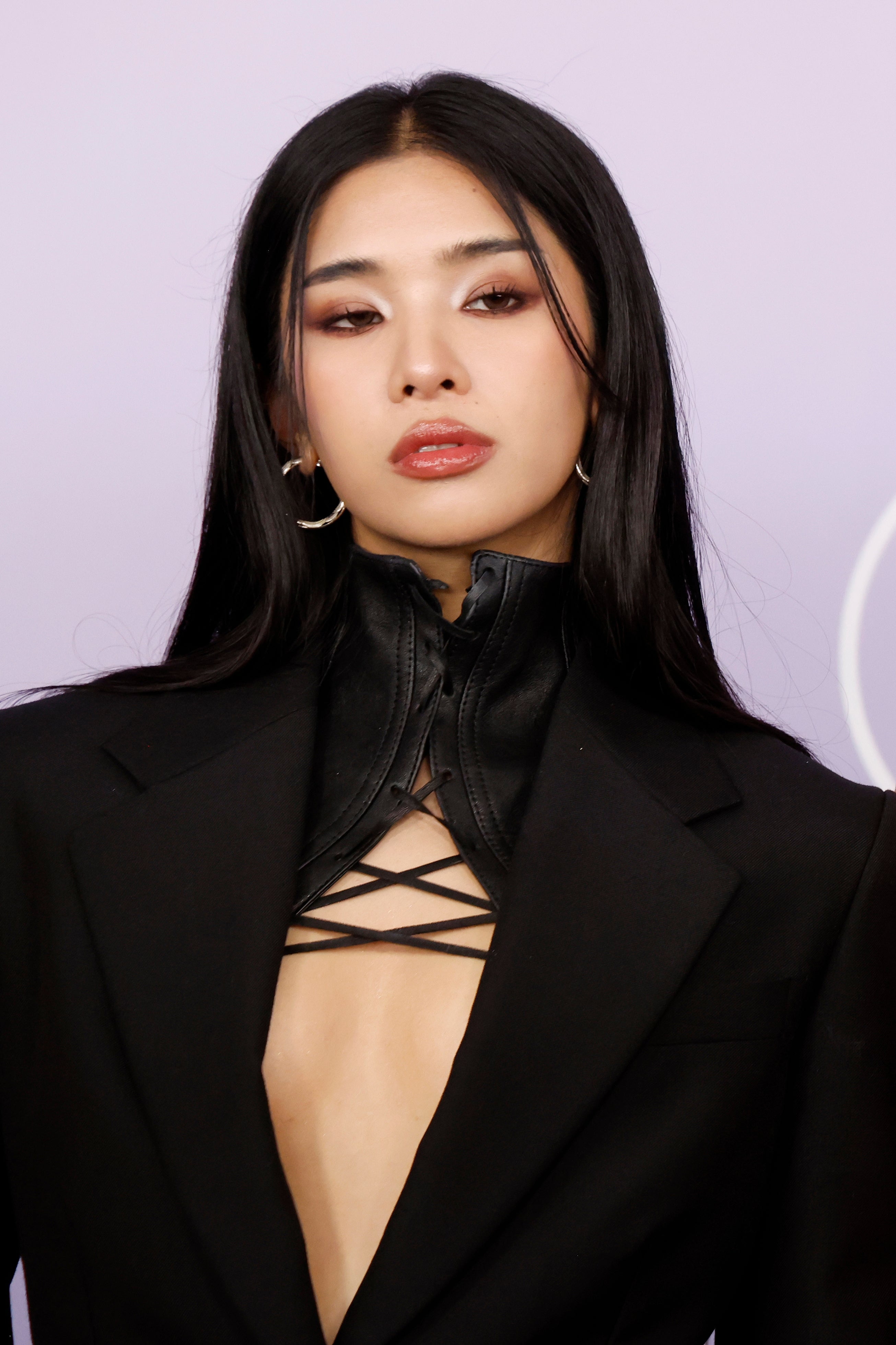 Person on the red carpet in an elegant black jacket with a high collar and crisscross detail, wearing statement earrings
