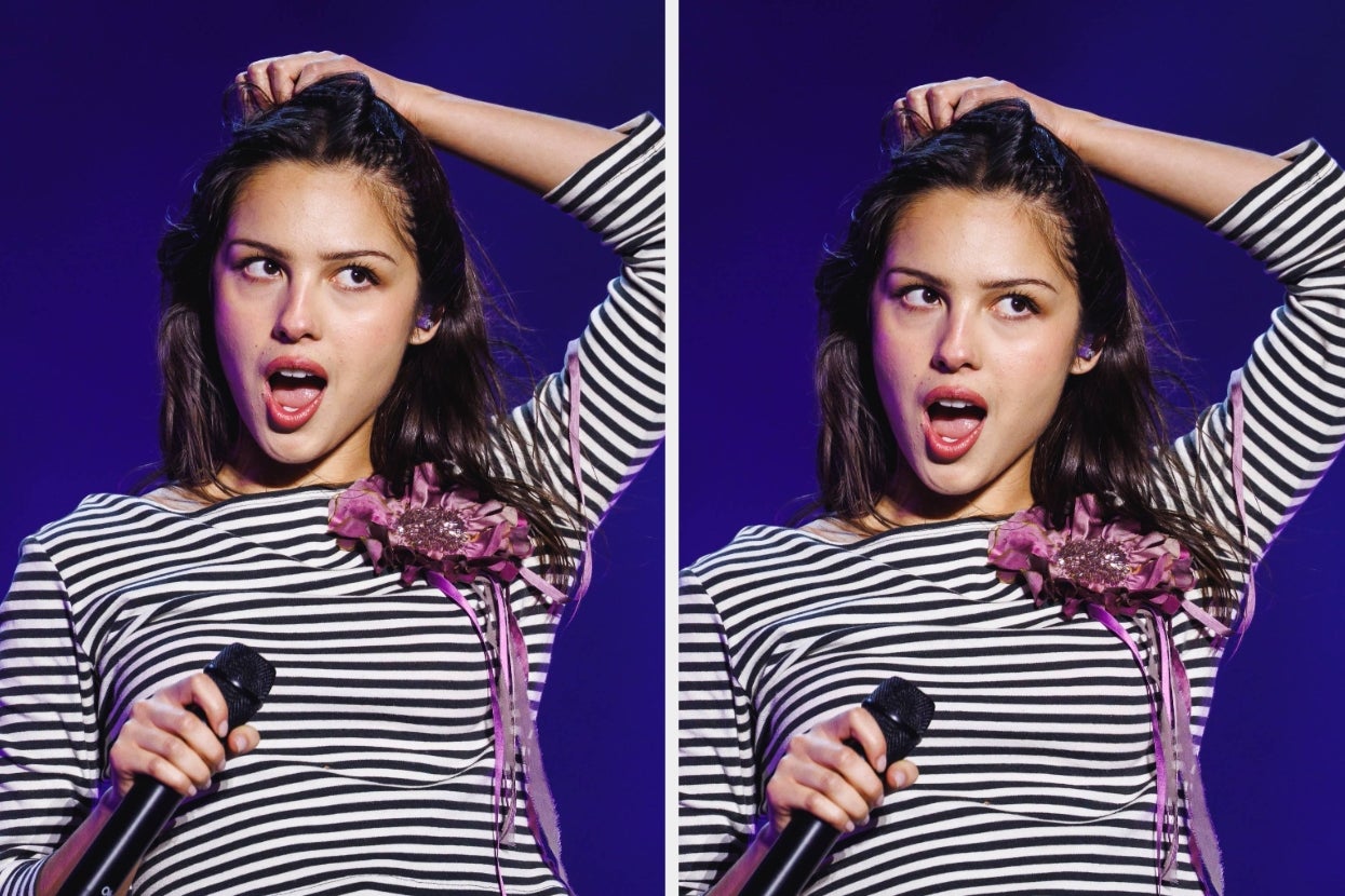 A person on stage with a microphone, wearing a striped outfit adorned with a decorative flower detail, striking expressive poses