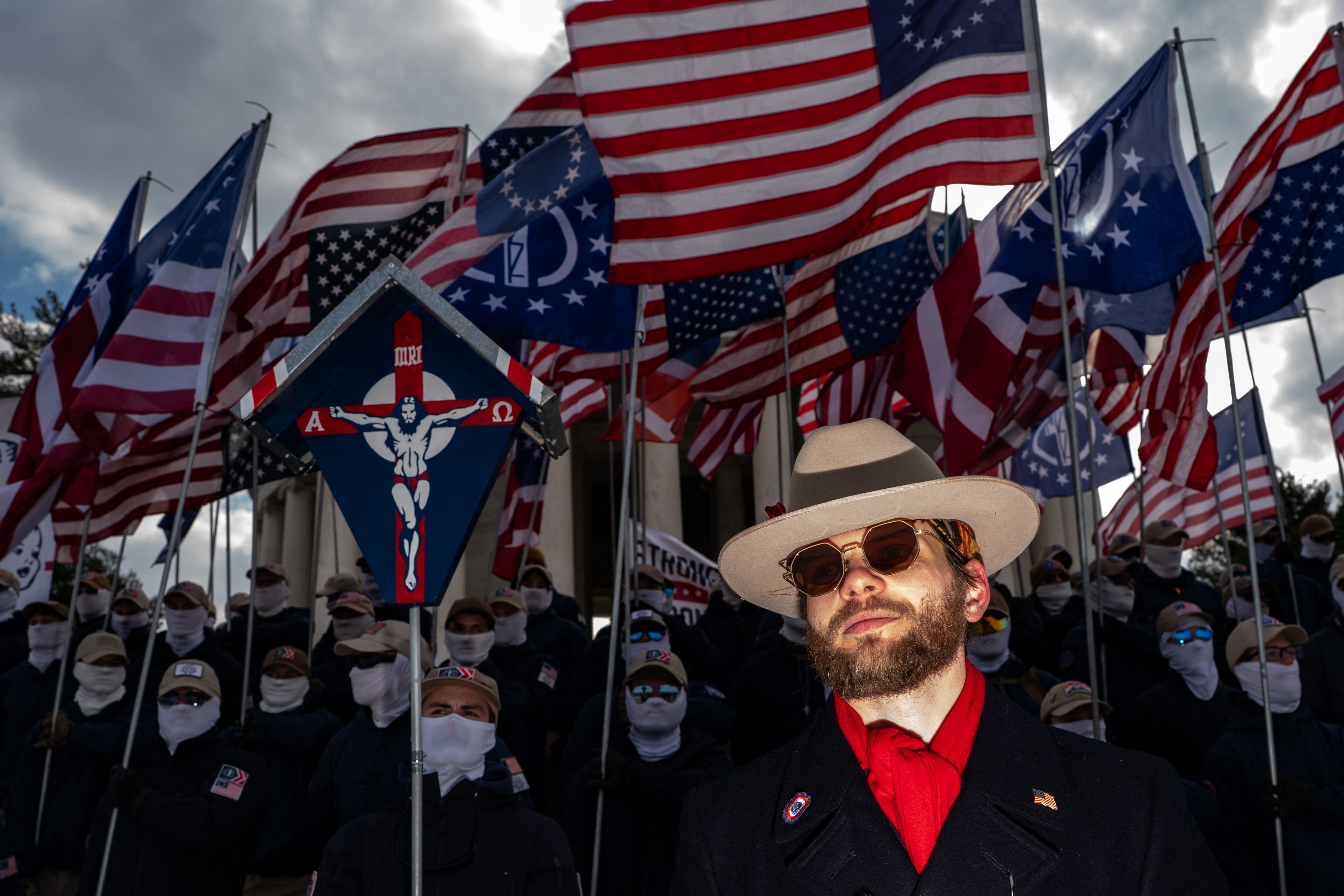 A idiosyncratic   successful  a suit   and chapeau  stands earlier  a radical  holding galore  American flags, wearing look   masks