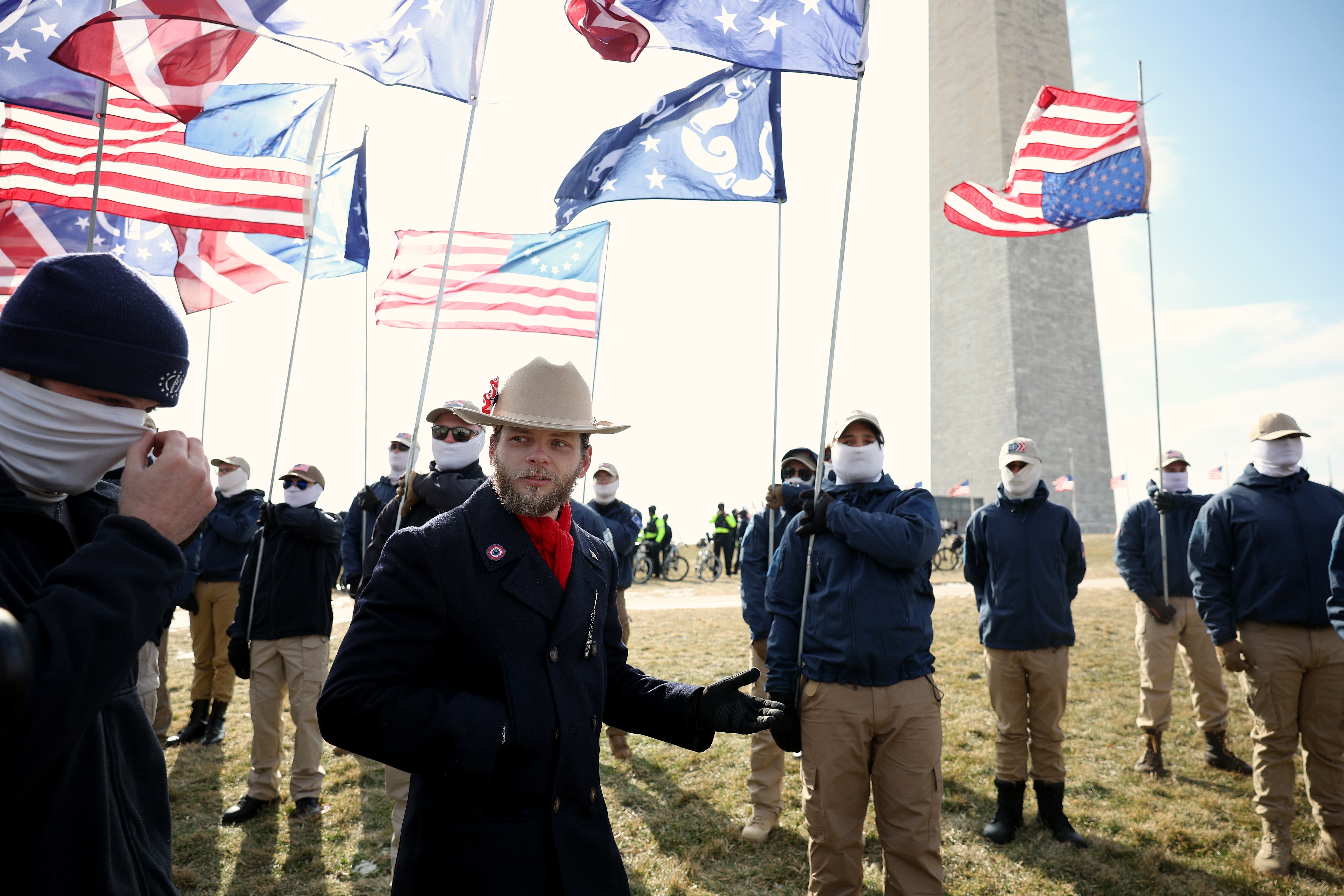 Group of radical   successful  coordinated outfits, with hats and masks, clasp  flags adjacent   a gangly  monument outdoors
