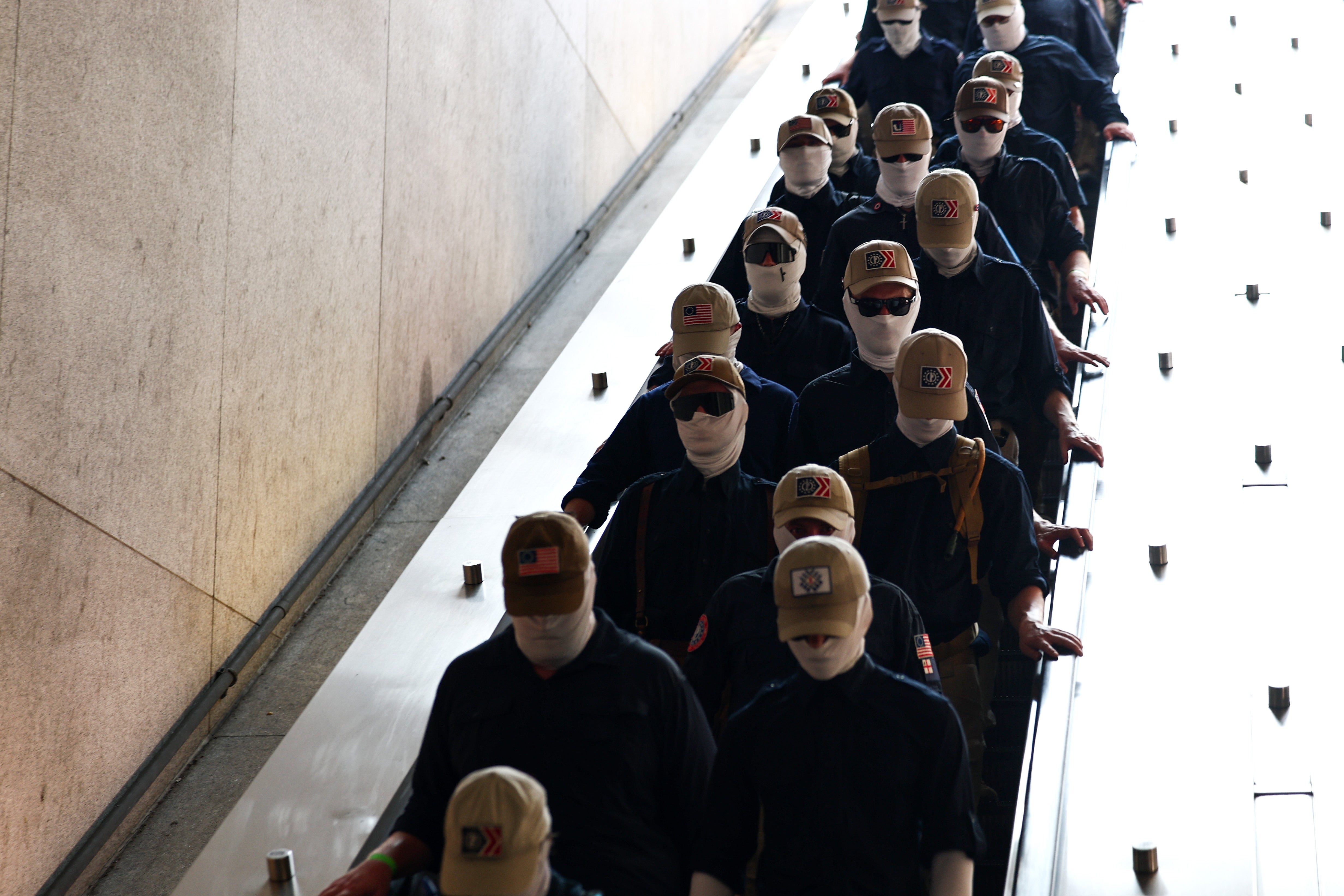 A radical  of radical   wearing identical hats, sunglasses, and look   coverings descending an escalator