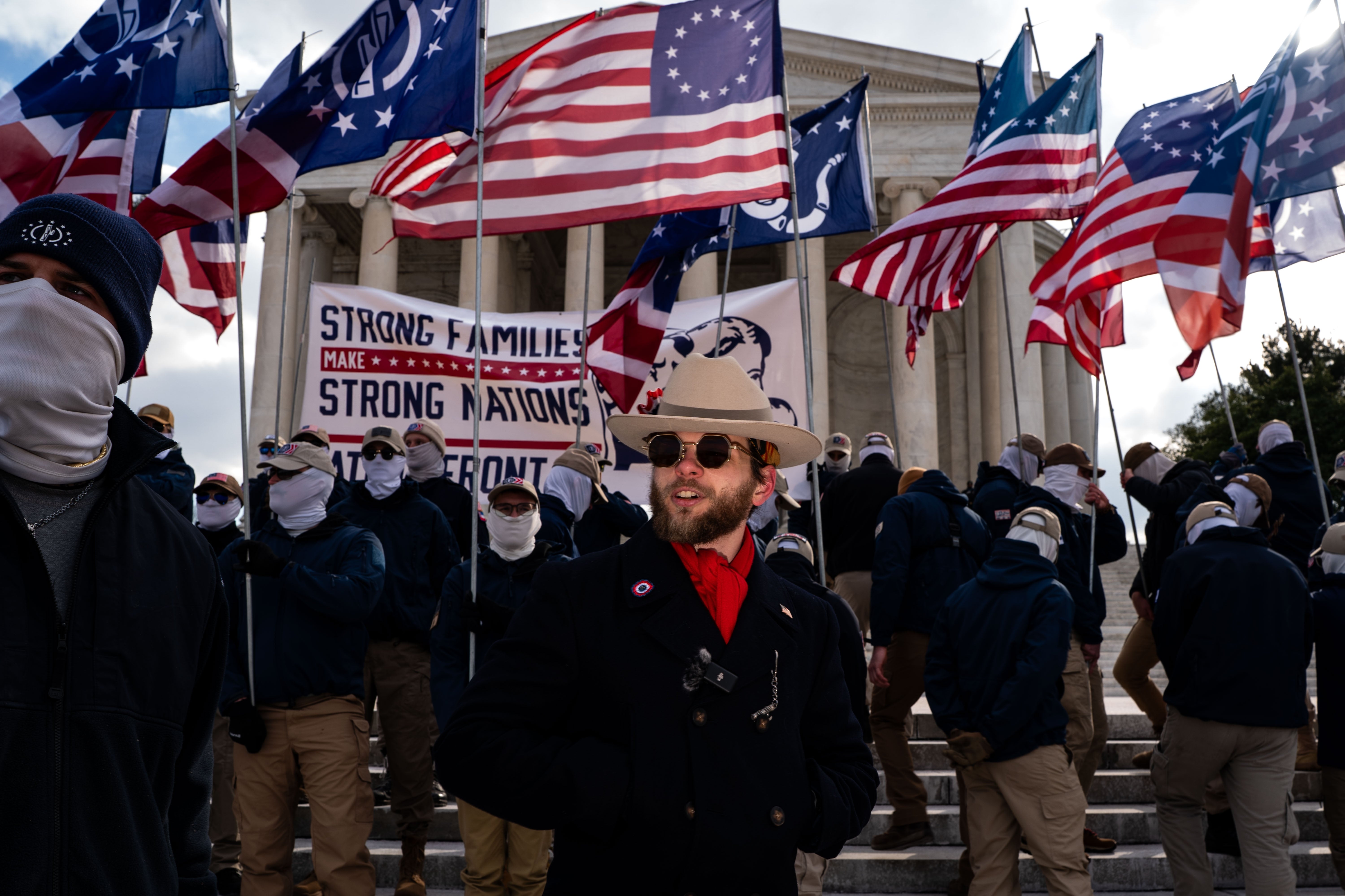 A radical  of individuals successful  look   coverings and khaki pants basal   successful  beforehand   of flags with American-themed designs, gathered adjacent   a ample  gathering  with columns
