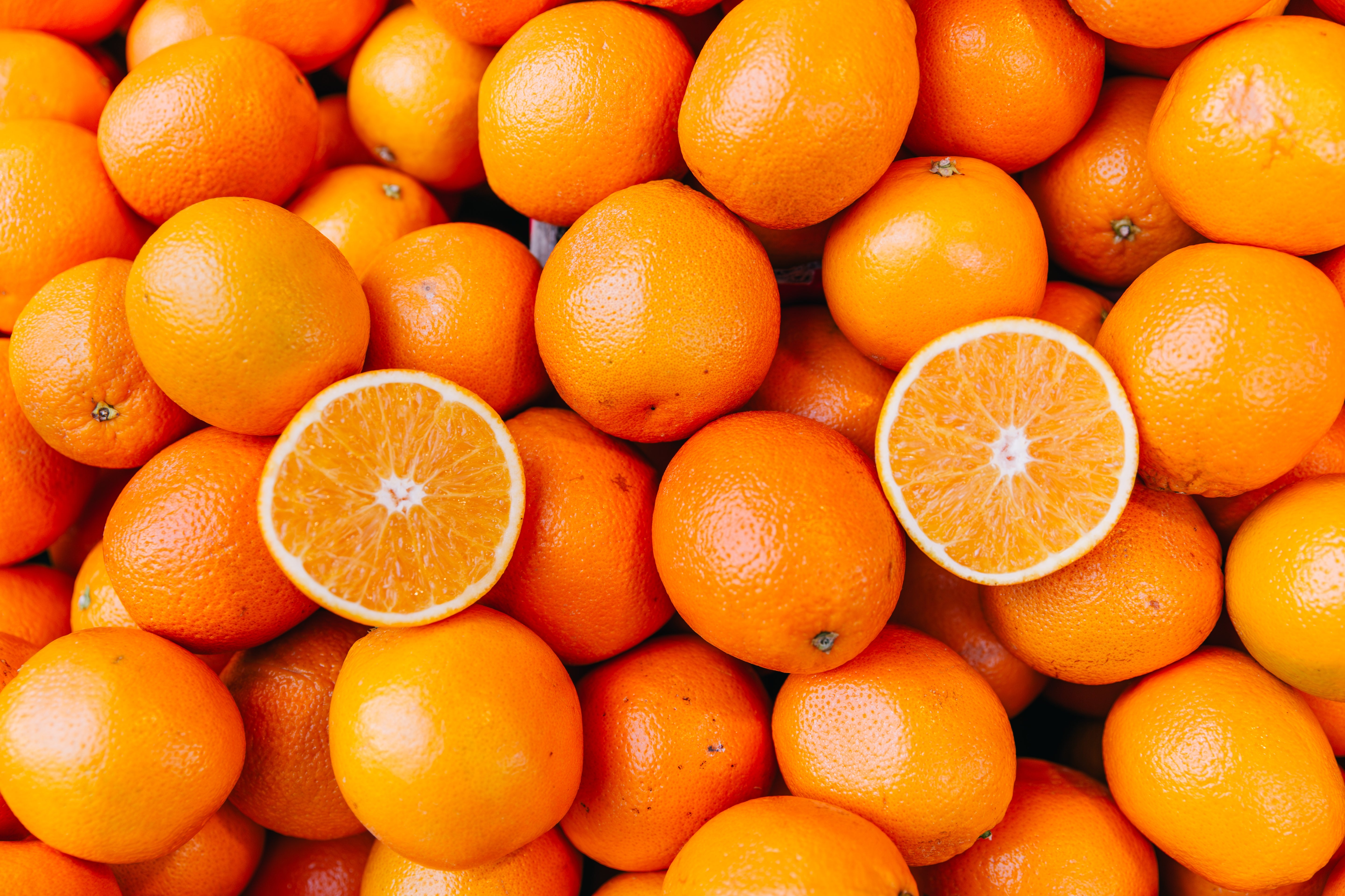 A heap of full oranges with 2 halves chopped to amusement the interior