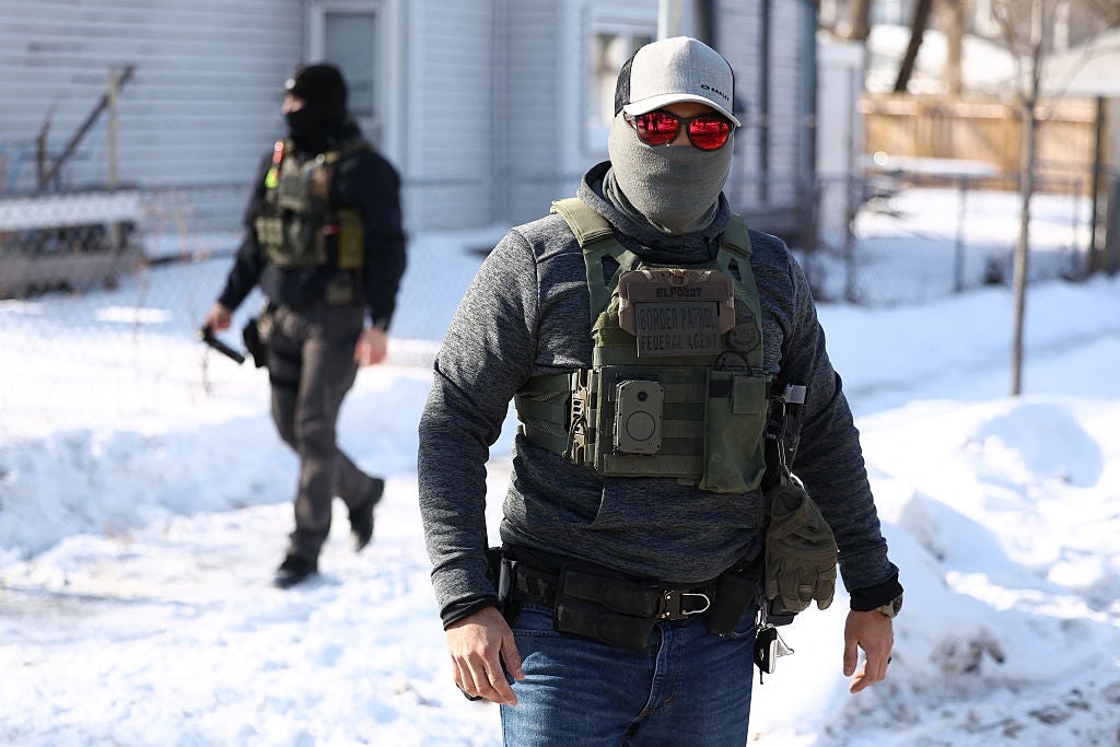 Two tactical officers, wearing masks and gear, patrol snow-covered vicinity  streets