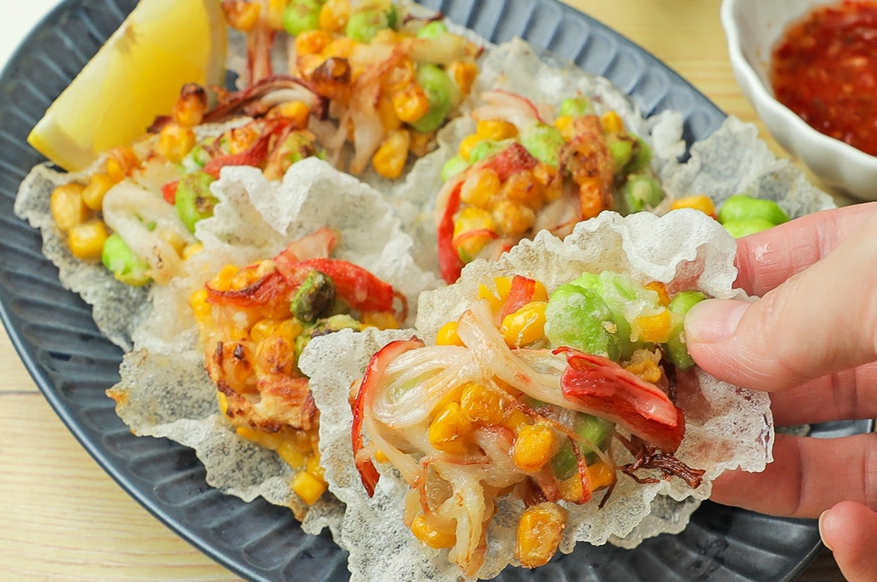 手に持ったライスチップスに、豆、トウモロコシ、カニがのせられている料理。横にディップ付き。
