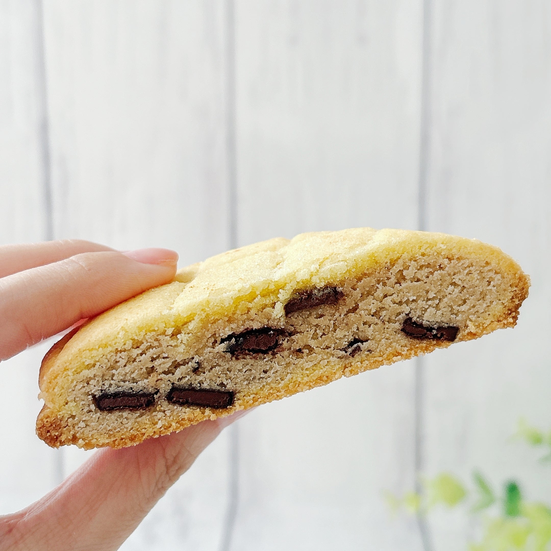 セブン-イレブンの「お店で焼いたメロンパンみたいなチョコクッキー」半分にカットしたクッキーを持ち上げている様子。