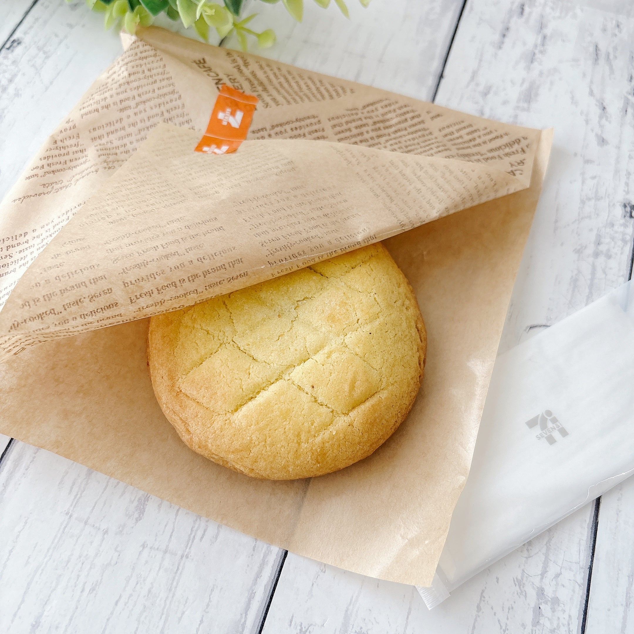 セブン-イレブンの「お店で焼いたメロンパンみたいなチョコクッキー」紙に包まれてテーブルの上に置かれている様子。