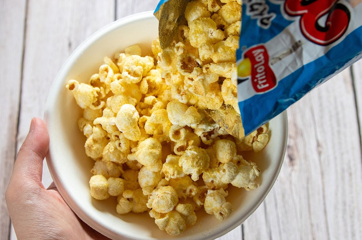 袋から白いボウルにポップコーンを注いでいる様子。手がボウルを持っている。