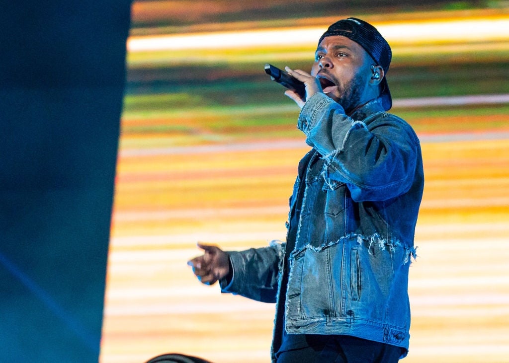 A performer sings energetically connected stage, wearing a distressed denim overgarment and a backwards cap