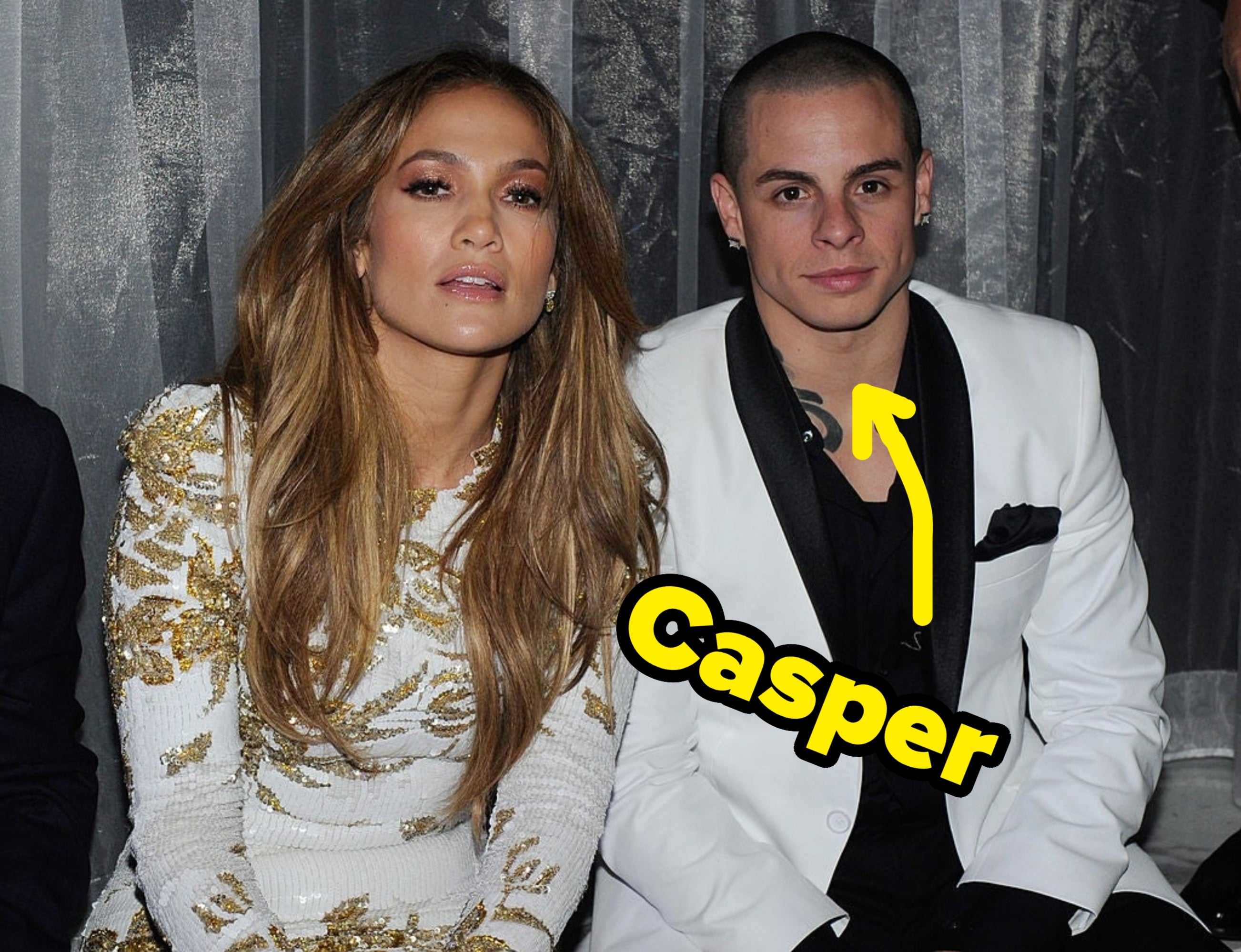 Two individuals are sitting together, 1 successful a achromatic formal with golden details and the different successful a achromatic overgarment with a achromatic shirt