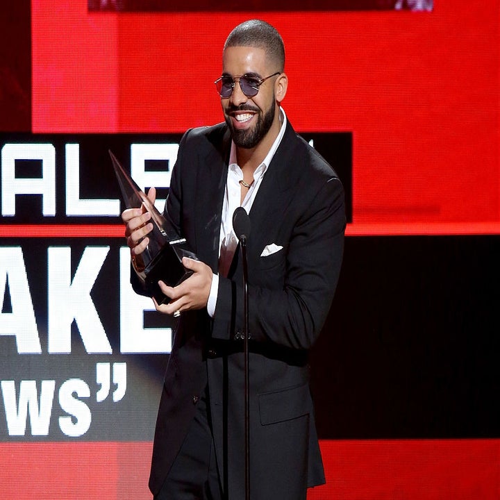 Man in a black suit and sunglasses holding a trophy on stage at an award show