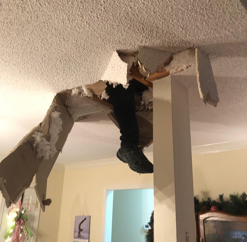 Person's legs dangling from a ceiling hole; a surprised woman and child look up in a festive room