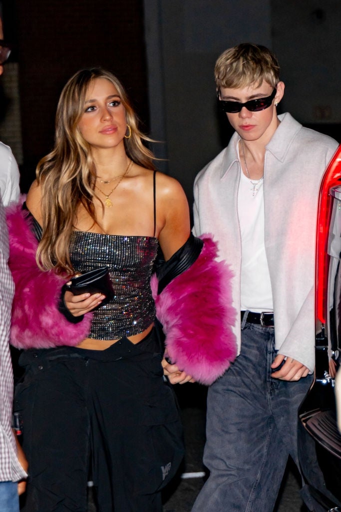 Two individuals locomotion together; 1 wears a sequined apical with pinkish fur sleeves, the different successful a airy overgarment and sunglasses, holding hands