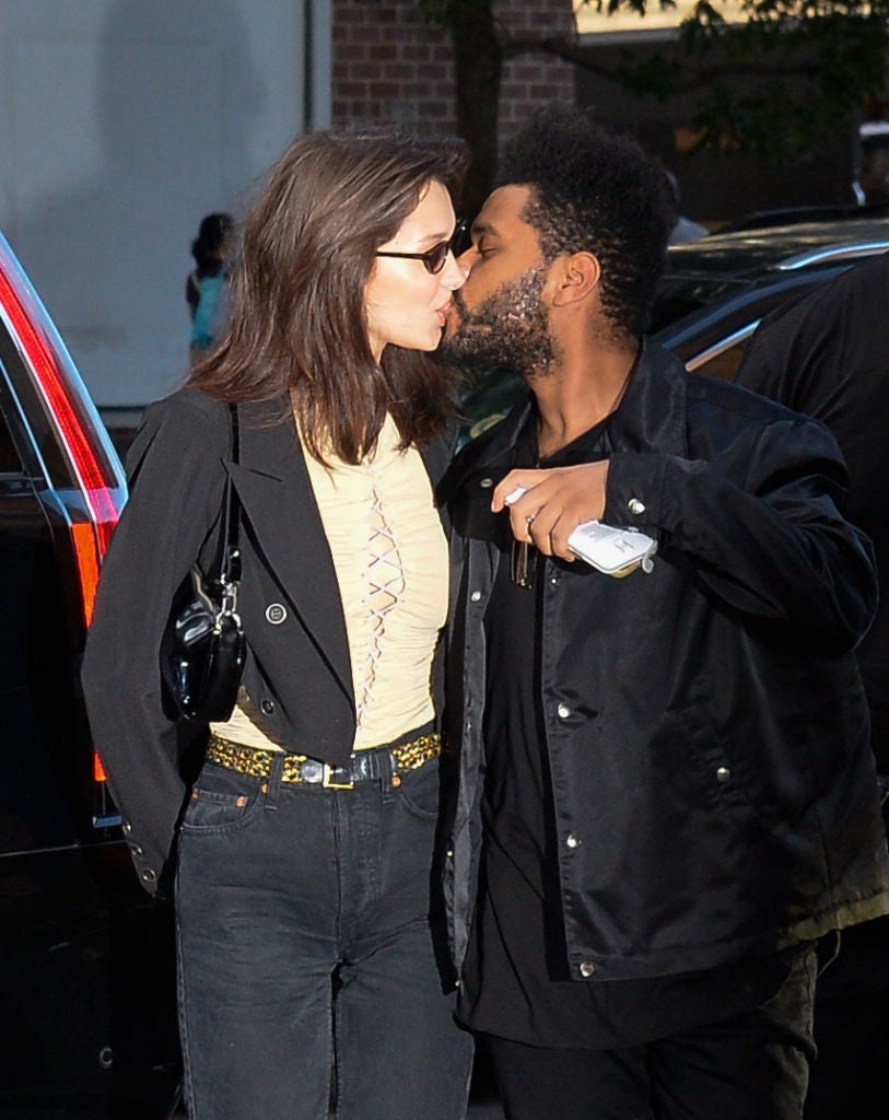 Two radical stock a buss connected the street. One wears a achromatic overgarment and apical with sunglasses; the different wears a acheronian overgarment and holds a phone
