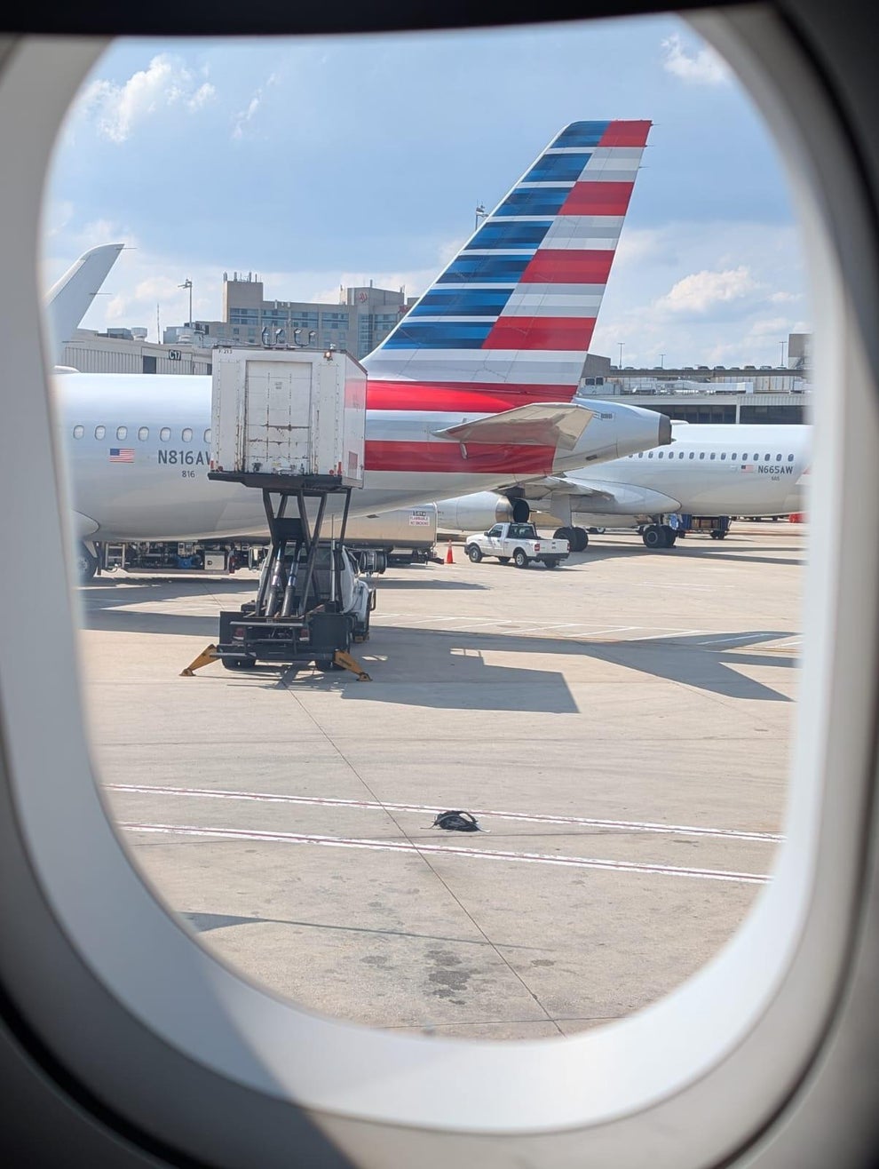 View from airplane window of a grounded aircraft, with its tail and luggage loader visible on the tarmac