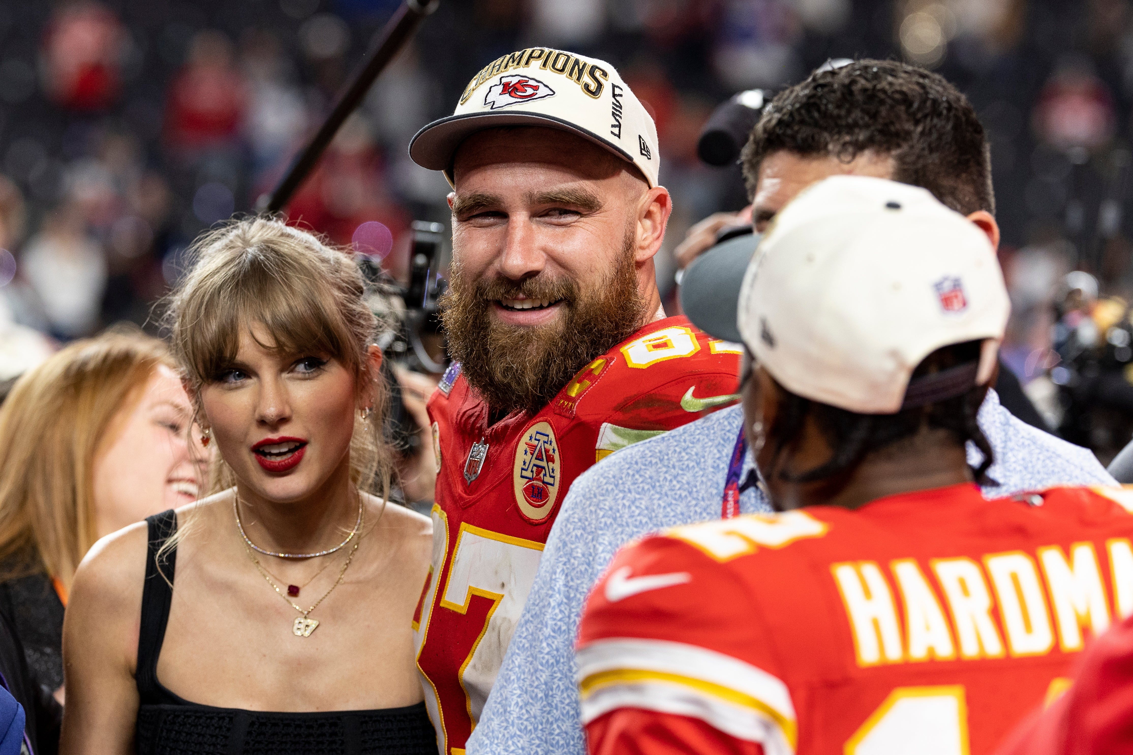 Taylor Swift successful a chic outfit stands alongside Travis Kelce wearing a shot jersey and a "Champions" cap, amidst a lively crowd