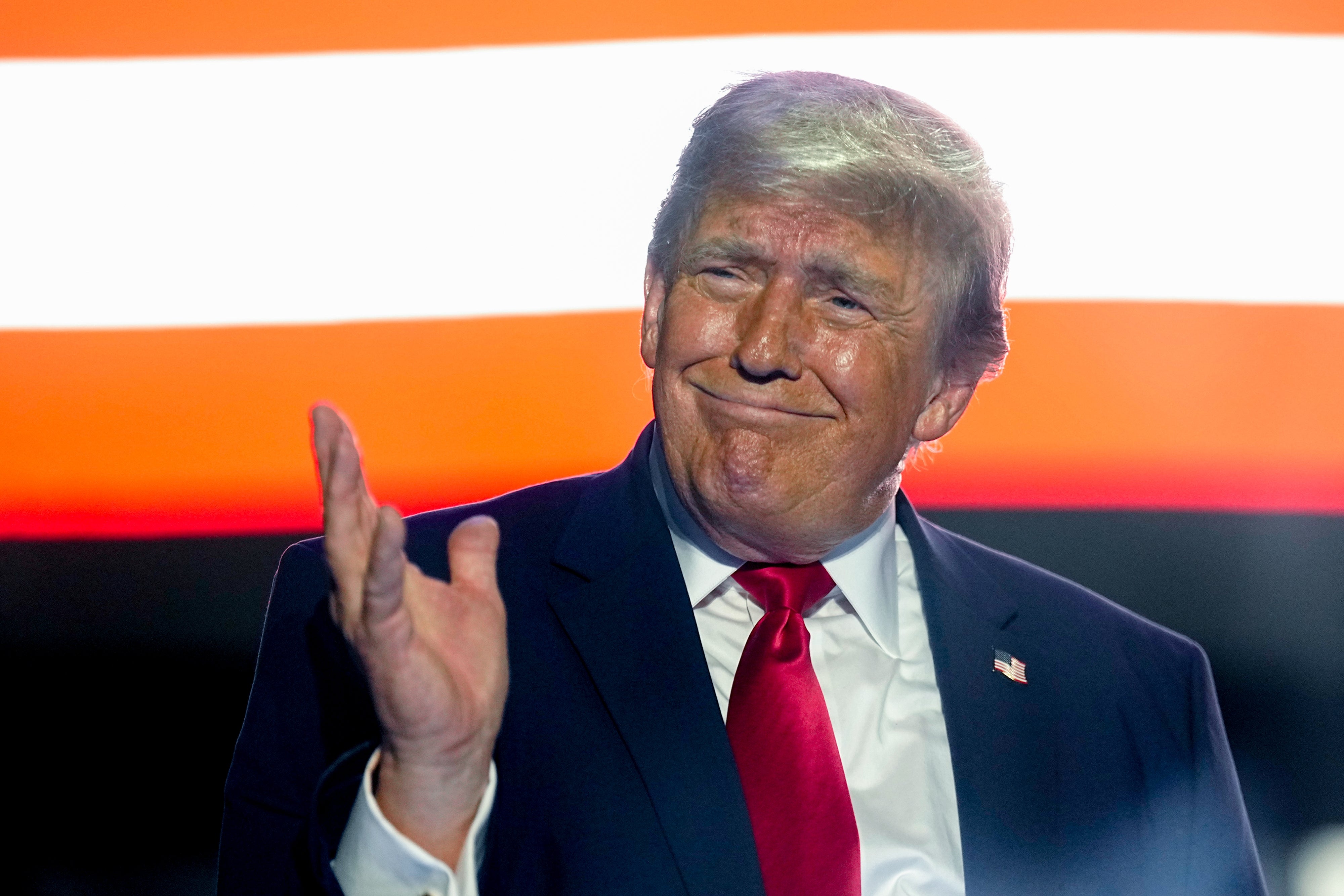 A idiosyncratic successful a suit, with a U.S. emblem pin, gestures with a manus raised. A portion of a emblem is disposable down them