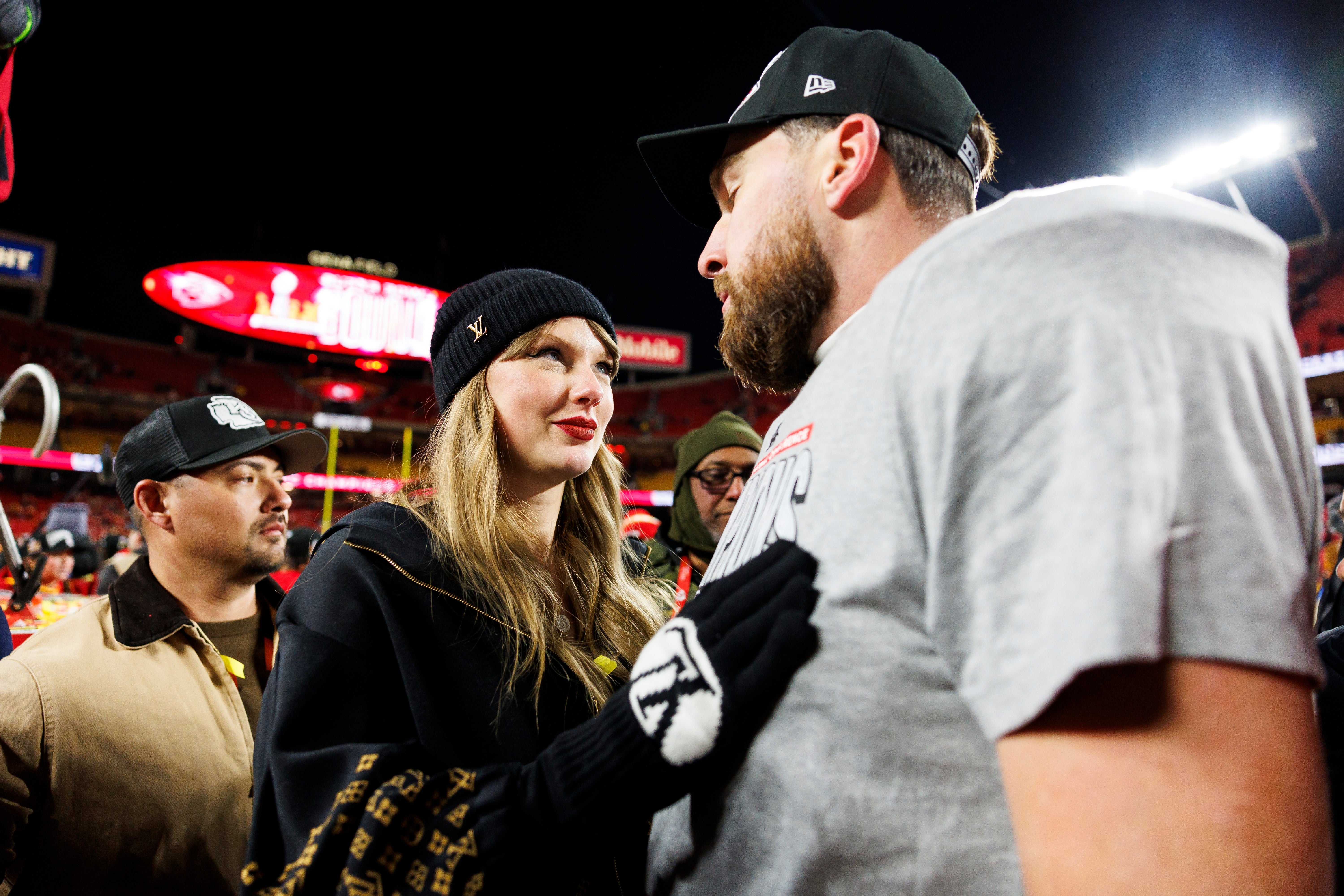 Taylor Swift successful casual attire with a beanie and gloves talks to Travis Kelce wearing a headdress and t-shirt astatine a sports event
